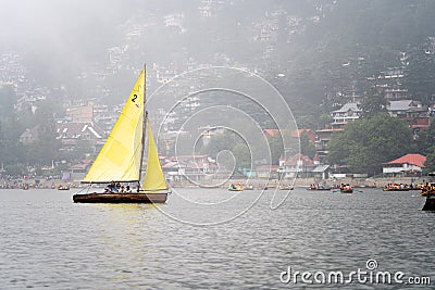 small colorful sailboat with people sitting on it passing row boats and pedal boats on a foggy day with buildings in the Editorial Stock Photo