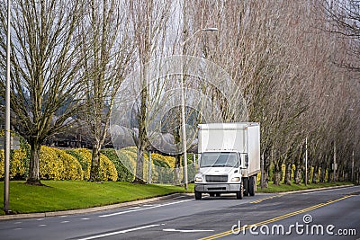 Small compact rig truck with box trailer transporting local goods on the city road with tree alley and railroad Stock Photo