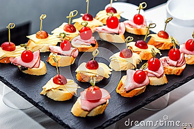 Small crostini with grilled baguette, cherry tomatoes, ham slices, cheese and fresh grapes on black background. Sandwiches or asso Stock Photo