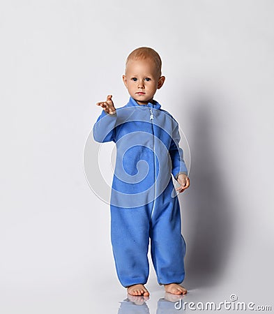 Small cute baby boy in blue warm comfortable jumpsuit standing and poitning at camera with hand Stock Photo
