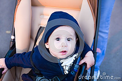 Small cute newborn baby boy sitting in a carriage in warm winter clothes with pacifier, concept of mothering autumn beanie, walk Stock Photo