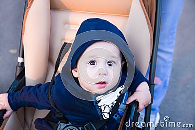 Small cute newborn baby boy sitting in a carriage in warm winter clothes with pacifier, concept of mothering autumn beanie, walk Stock Photo