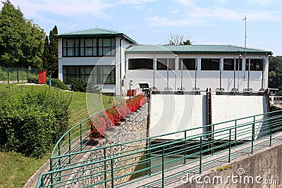 Small dam used to regulate and direct water to hydropower plant with freshly cut grass and flowers in front Stock Photo