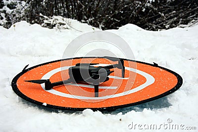 A small drone on its landing base among the cold white snow in the mountains in winter Stock Photo