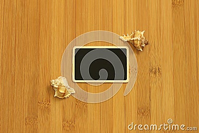 Small empty slate in width to write a message posed on the ground bamboo brown with beach shells on the sides Stock Photo