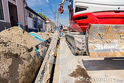 Small excavator with front blade is carry long HDPE pipe over trench, water supply network Stock Photo