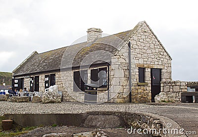 A small family enjoy coffee at the shop and visitor centre at the beautiful Ballintoy harbor on the North Coast of County Antrim i Editorial Stock Photo