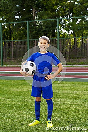 A small football player with a ball stands on a green football field Stock Photo