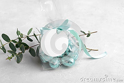 Small gift with chocolate easter eggs in a plastic bag with a bow of mint color ribbon and a round white gift tag mockup Stock Photo