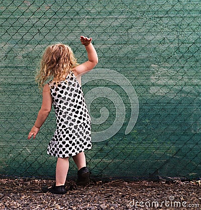 Small girl banging on a green fence Stock Photo