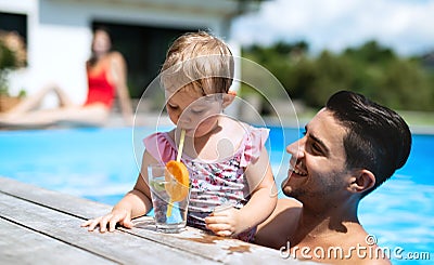Small girl with father drinking lemonade in swimming pool outdoors in backyard garden. Stock Photo