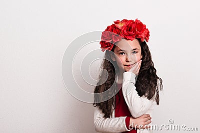 A small girl with flower headband standing in a studio, chin resting on her hand. Stock Photo