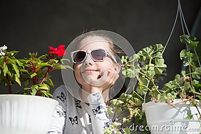 Small girl with flowers. Fashion child wear sunglasses on sunny day. Beauty kid with plant pots in summer or spring. Freshness and Stock Photo