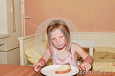 Small girl has a snack. Little girl eats bread spread with cheese. Cute girl in kitchen. Family and childhood concept. Stock Photo