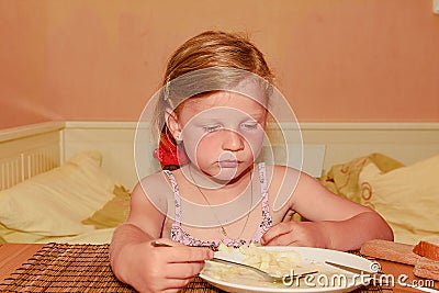 Small girl has a snack. Little girl eats bread spread with cheese. Cute girl in kitchen. Family and childhood concept. Stock Photo