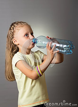 Small girl with luxurious long hair drinks water from bottle, on grey Stock Photo