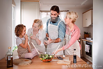 A small girl with parents and grandmother at home, preparing vegetable salad. Stock Photo