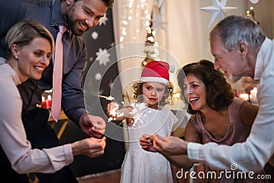 Small girl with parents and grandparents indoors celebrating Christmas, holding sparklers. Stock Photo