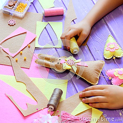 Small girl shows a felt bunny in hands. Girl made a felt cute bunny with hearts for Easter. Tools and materials for kids Stock Photo