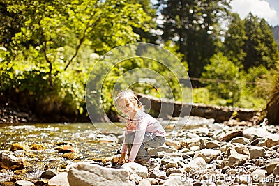 Small girl sit on rocks shore of mountain river Stock Photo