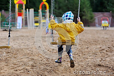 Small girl in yellow rain coat on swing Stock Photo