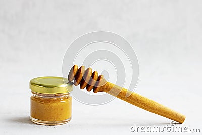 Small glass jar with metal cap with light yellow honey and special wooden spoon isolate on grey cement background with Stock Photo