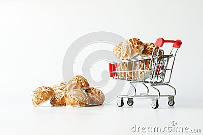 Small glazed cupcakes in a miniature supermarket cart. The concept of buying sweets in a bakery and delivering groceries. White Stock Photo