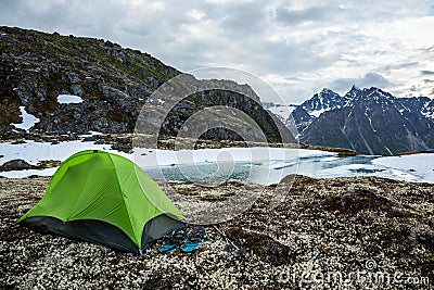 Small green backpacking tent with snowshoes outside. Overlooking partially frozen lake in spring time Stock Photo