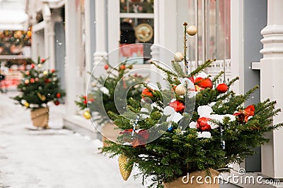 Small green Christmas trees in pots with balls, toys and snow on the new year square near houses on a blurred background Stock Photo