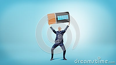 A small happy businessman smiles and holds a huge fully charged battery over his head. Stock Photo