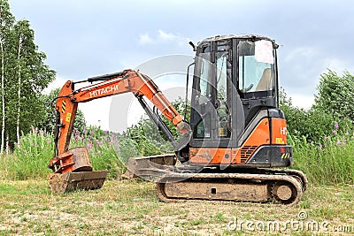 Small Hitachi Excavator on empty green area for construction in countryside in summer, side view Editorial Stock Photo