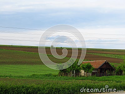 A small house surrounded by green field grass and tilled field. Ploughed cultivated ground. Countryside. Stock Photo