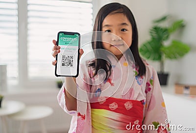 Small japanese child with traditional costume showing covid-19 vaccination certificate on smartphone. Stock Photo
