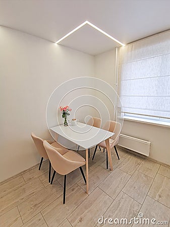 Small kitchen corner with white walls, a dining table and beige armchairs. Vase with roses as an element of interior Stock Photo