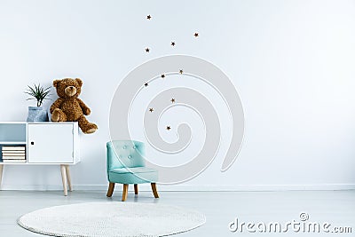 Small light blue armchair for kid standing in white room interior with stars on the wall, white rug and cupboard with Stock Photo