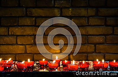 Small lighted candles in red glass candlesticks in front of a brick wall Stock Photo