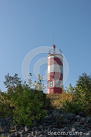 A small lighthouse stands on a cape among trees and bushes Stock Photo