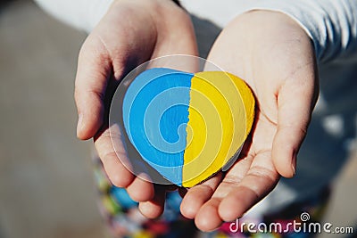 Small little kid hold heart shaped stone with Ukraine national flag or anthem Stock Photo