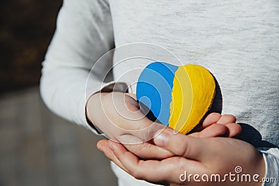 Small little kid hold heart shaped stone with Ukraine national flag or anthem Stock Photo