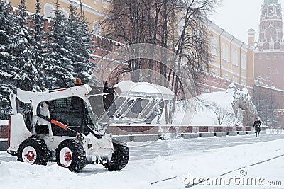 A small loader excavator bobcat removes snow from the sidewalk near the Kremlin walls during a heavy snowfall Editorial Stock Photo
