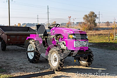 Small mini glamour modern pink new tractor with trailer standing near hangar building farm countryside during sunset or Editorial Stock Photo