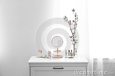 Small mirror and different makeup products on chest of drawers Stock Photo