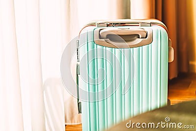 Small modern luggage with two-tone color, front view, stand on the wooden floor in a hotel room, background of white curtain, Stock Photo