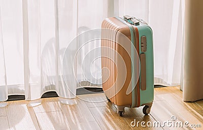 Small modern luggage with two tone color, stand on the wooden floor in a hotel room, background of white curtain, space for text Stock Photo