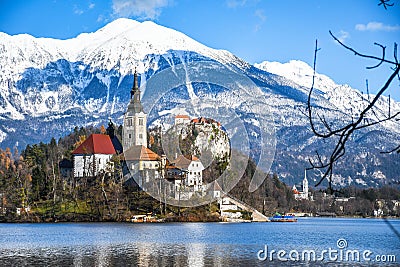 Small natural island in the middle of alpine lake with church dedicated to assumption of Mary and castle with snowy mountains Stock Photo