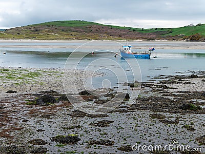 A small old fishing boat is anchored, shallow water at low tide on a cloudy day. Hills under a cloudy sky. Silt Stock Photo