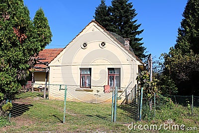 Small old suburban family house with two windows and decorative attic ventilation openings surrounded with rusted metal fence Stock Photo