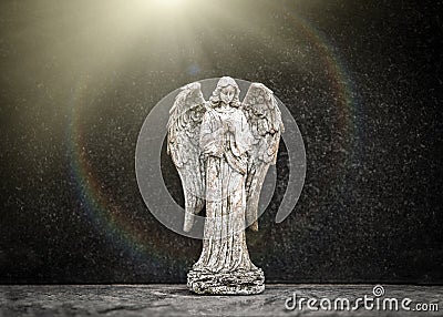 Small old weathered stone weeping angel with wings ornament standing in sorrow on black granite grave headstone in peaceful church Stock Photo