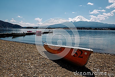 Small orange boat is visible on the shore of a tranquil lake in Fujikawaguchiko, Japan Editorial Stock Photo