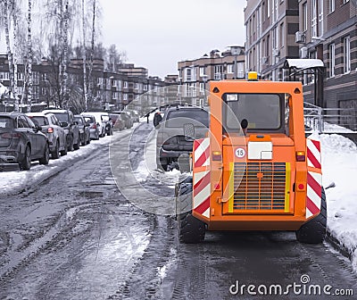 A small orange snowplow removes melted snow from the driveway Stock Photo